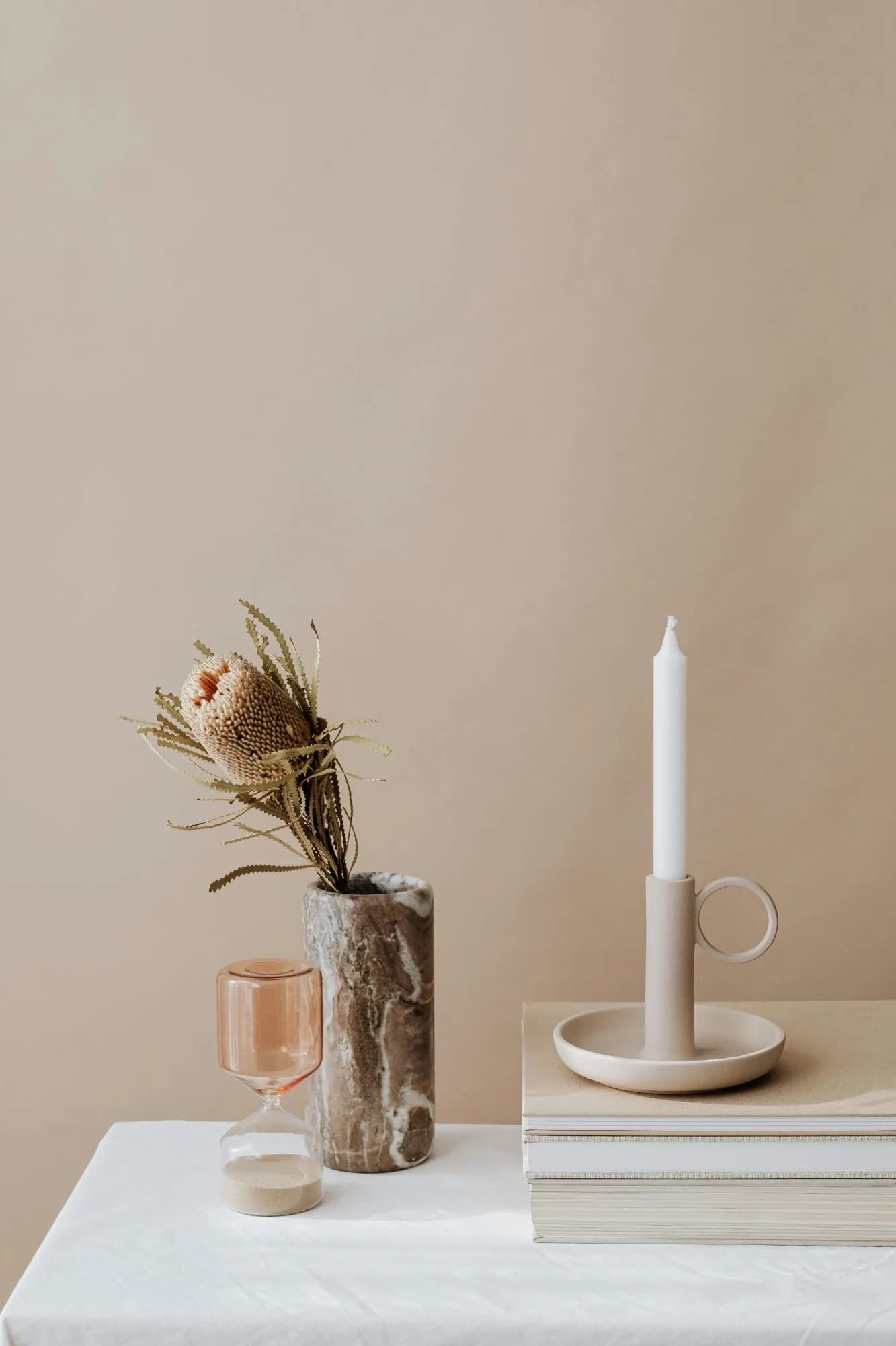 Kerze, Trockenblumen und eine Sanduhr auf Büchern vor einer hellen Wand
